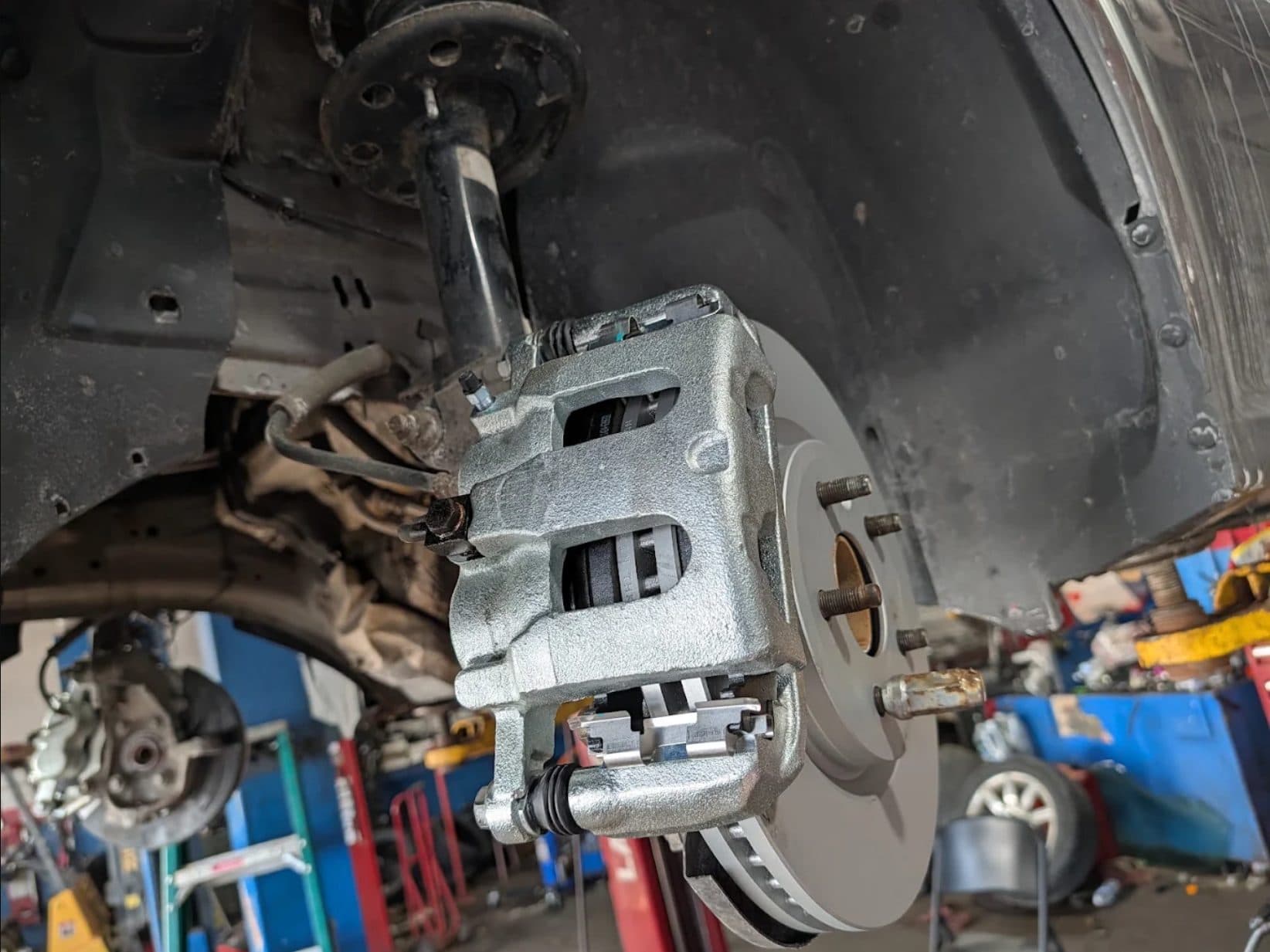 A newly fitted brake caliper and rotor on a vehicle raised on the lift
