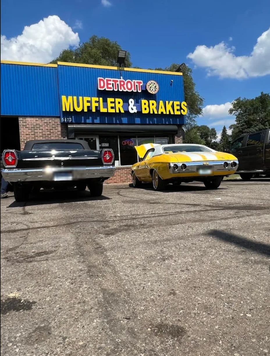 Two classic muscle cars parked outside Detroit Muffler & Brakes