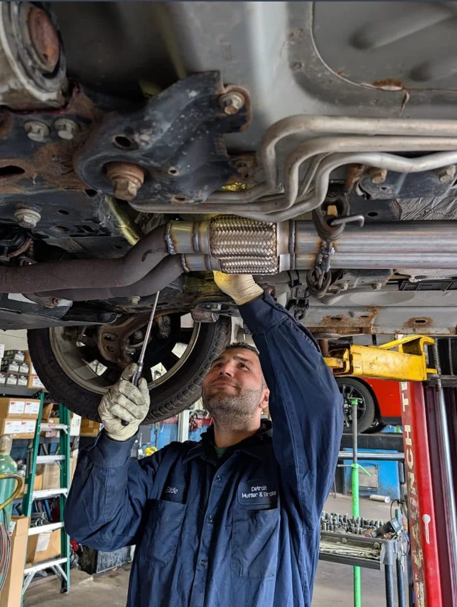 A Detroit Muffler & Brakes technician in a branded shirt working under a vehicle
